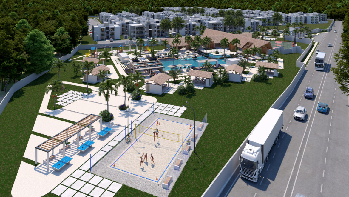 Aerial view of a resort-like community with a large pool, cabanas, palm trees, playground, and apartment buildings surrounded by greenery and a road with vehicles nearby.