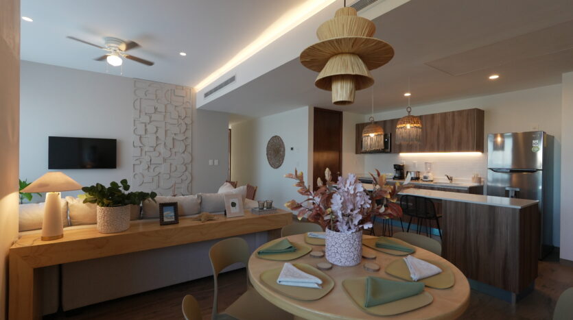 Open-concept living area with a round dining table, pastel napkins, and woven pendant lights over the kitchen island.