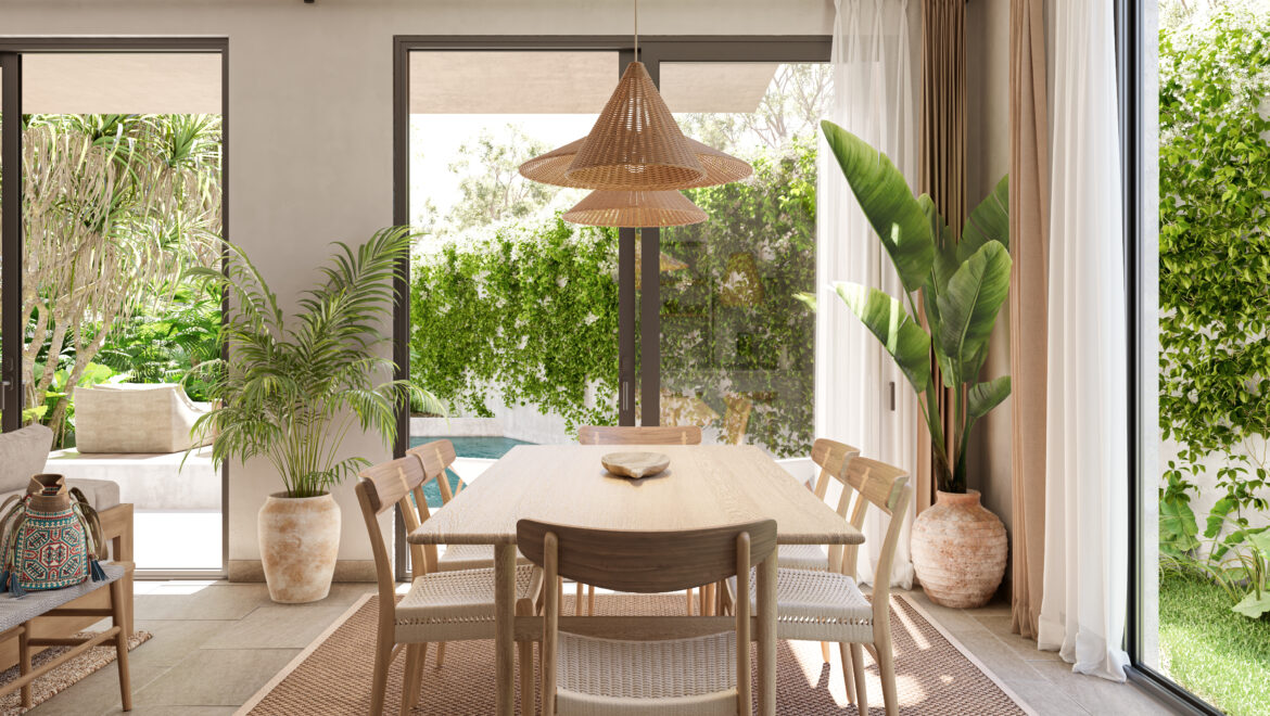 Dining room with a wooden table and chairs, a woven pendant light, and abundant greenery visible through large glass doors.