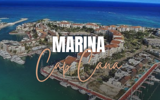 Aerial view of Cap Cana Marina with yachts docked along piers and turquoise water behind the townhouses and hotels.