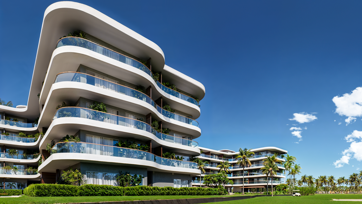 Modern white apartment building with curved glass balconies and greenery against a clear blue sky.