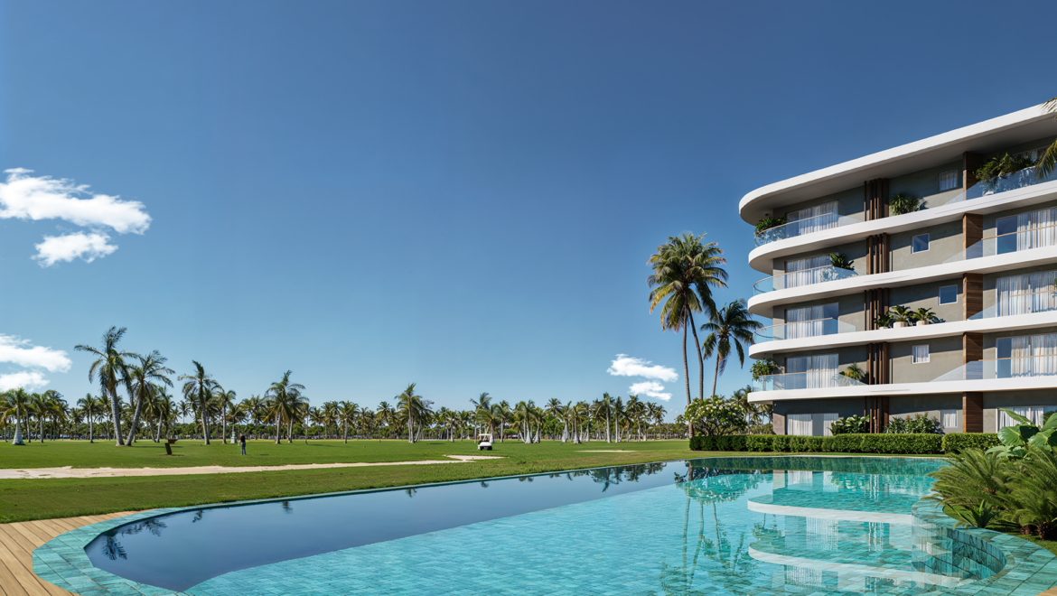 Modern curved apartment building beside a palm-lined lawn and clear blue sky by a turquoise pool.