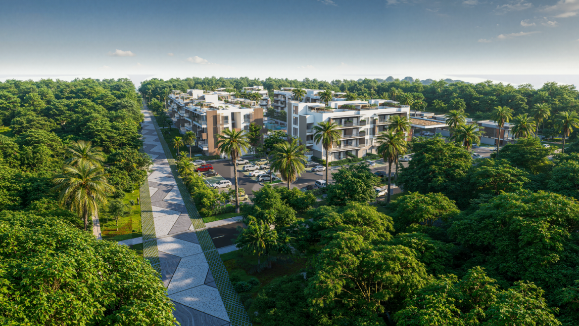 Aerial view of modern white apartment buildings surrounded by dense tropical trees and palm trees, with a patterned pedestrian path and parked cars nearby.