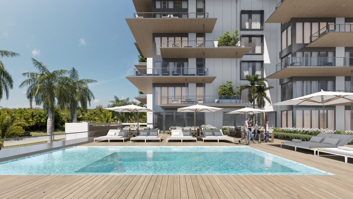 Modern apartment complex with a large pool, wooden deck, loungers, and white parasols. People stand near the poolside.