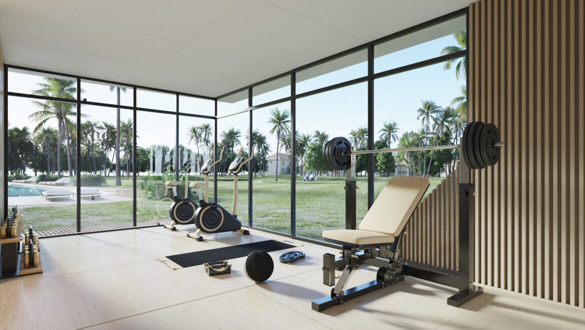 Spacious gym with large glass walls overlooking palm trees; cardio machines and free weights inside.