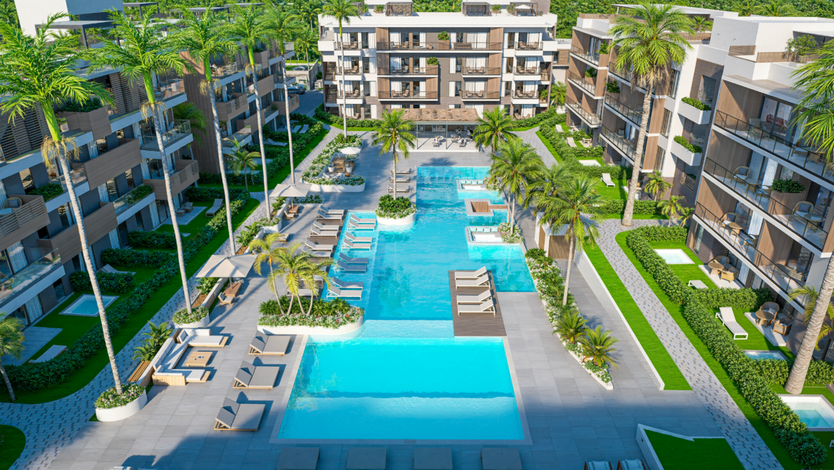 A resort pool area surrounded by modern white and wood-clad buildings, palm trees, lounge chairs, and green landscaping.