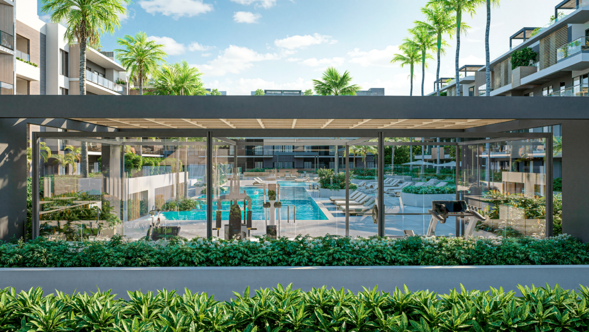 Glass-walled fitness center in a tropical resort-like complex, overlooking a large outdoor pool with lounge chairs and palm trees.