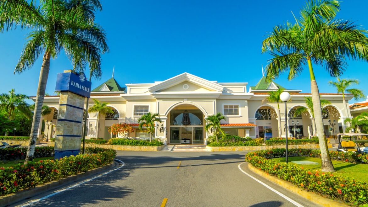 Bahia Mall entrance framed by palm trees under a bright blue sky, with a landscaped roundabout and signage.