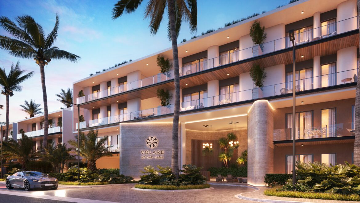 Facade of a modern hotel with balconies, palm trees, and warm evening lighting; sign reads 'Volare at Cap Cana'