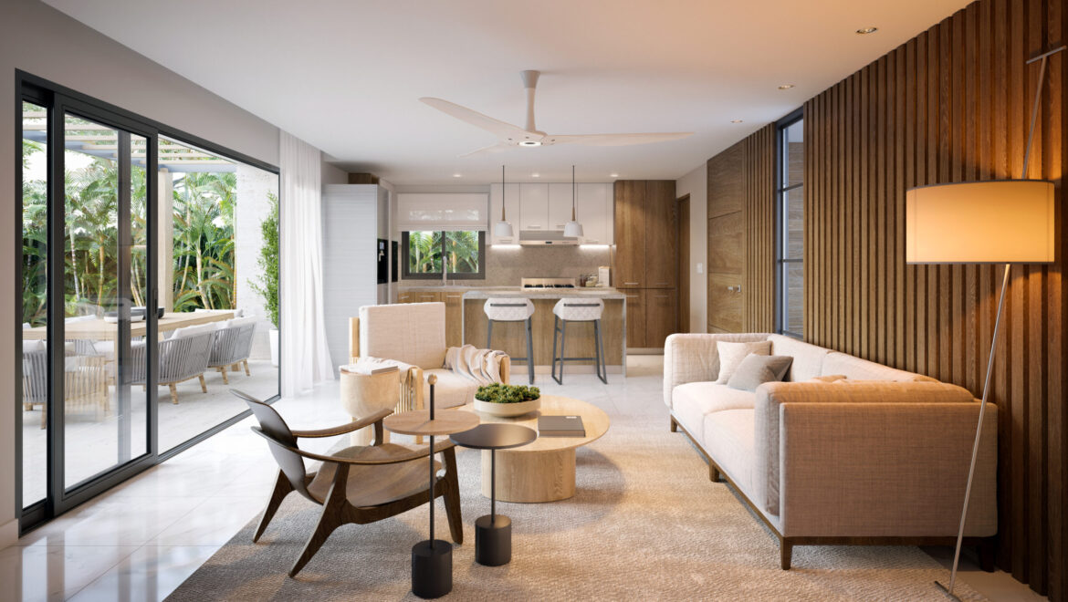Open-concept living room with beige sofa, wood slat wall, and kitchen in background; glass patio doors reveal outdoor seating.