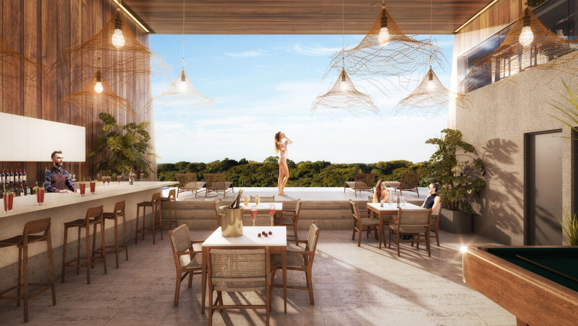 Outdoor bar terrace with wooden walls, wicker chairs, and hanging light sculptures; a bartender serves drinks while guests sit at tables and a woman in a bikini stands on a poolside platform overlooking greenery.
