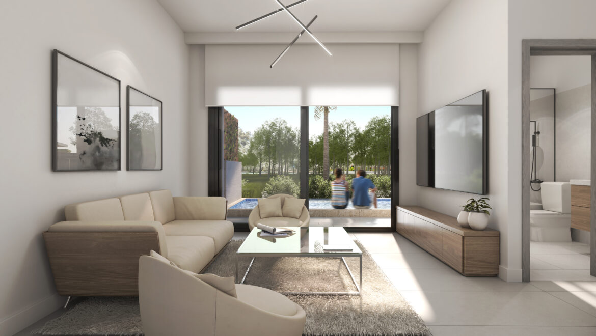Bright modern living room with beige sectional, glass coffee table, wall-mounted TV, and large glass doors opening to a garden. Two people walk outside by greenery and a pool view.