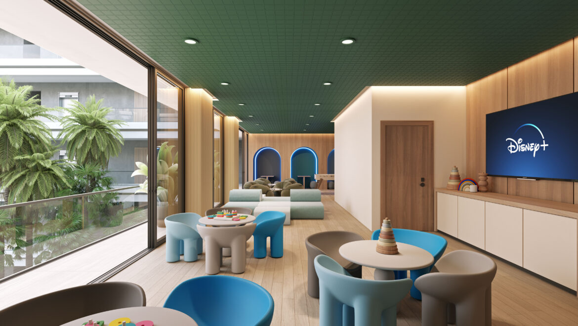 Indoor kids' play area with round tables, blue and gray chairs, and a Disney+ screen on a wooden wall. The space has large glass walls and greenery outside.
