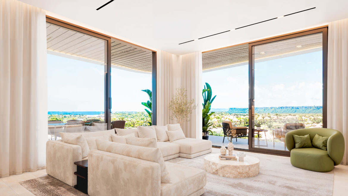 Bright living room with a large white sectional, neutral rug, and glass doors opening to a seaside view.