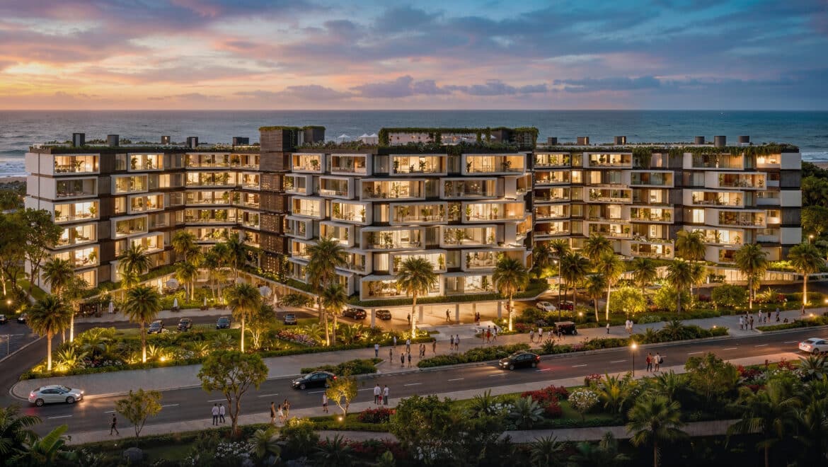 Modern waterfront apartment complex lit up at dusk, with balconies facing the ocean and palm trees in the foreground.