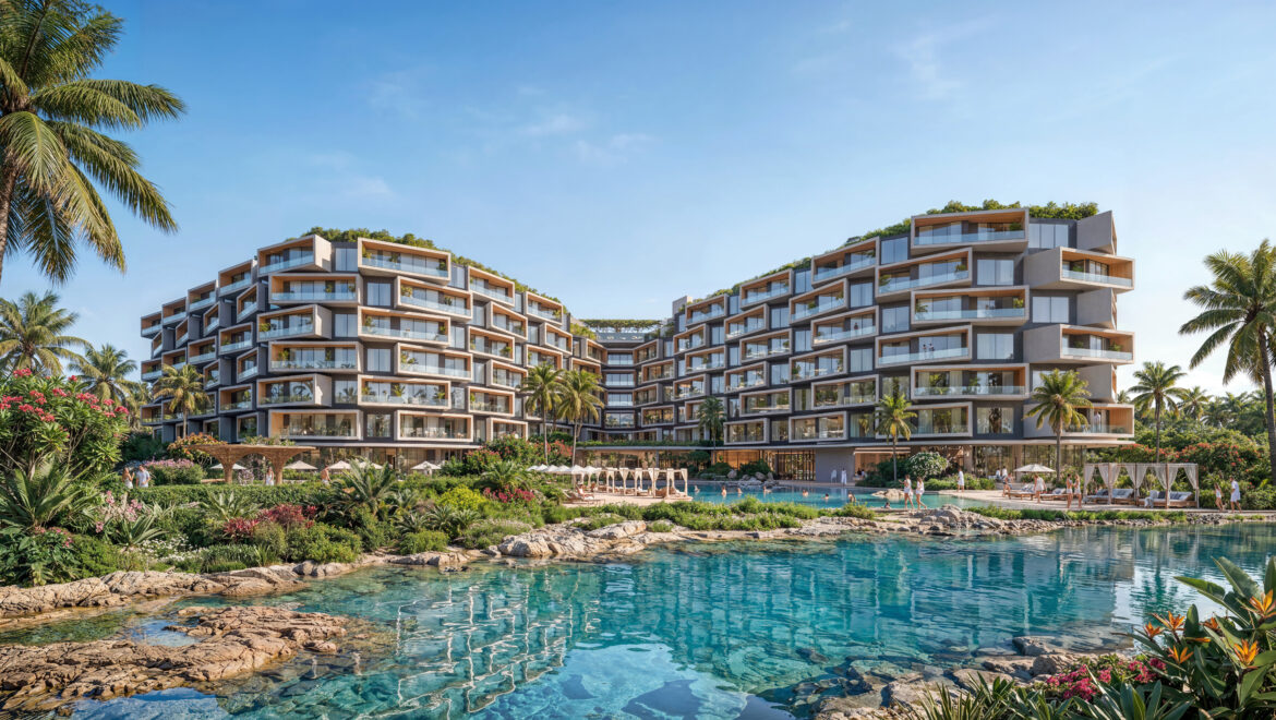 Modern resort buildings with stacked balconies surround a central pool area amid tropical landscaping and palm trees by turquoise water.