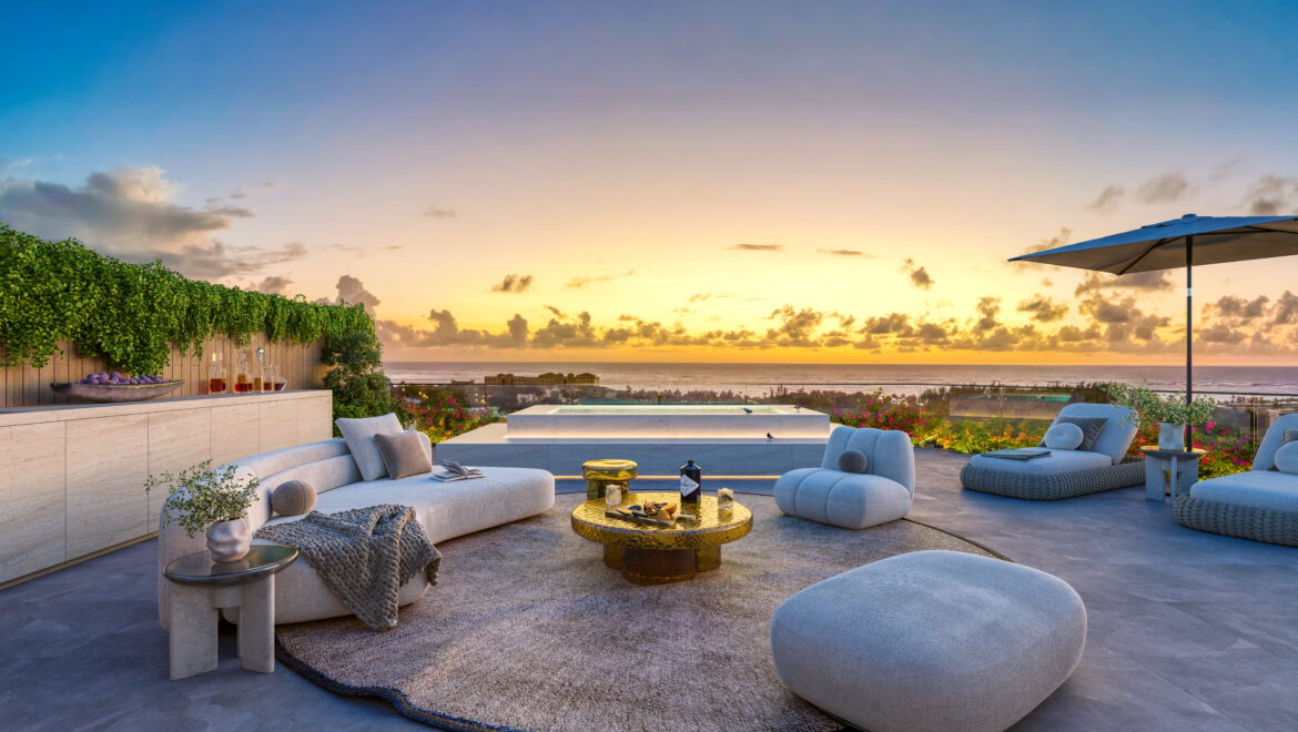 Modern outdoor lounge by the sea at sunset, with gray sectional sofas, round woven table, and a large umbrella.