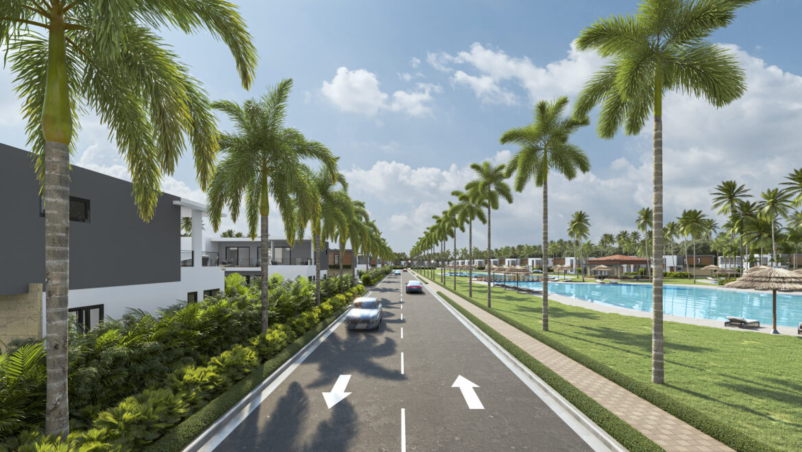 Wide resort street with palm trees, modern buildings on left, and a pools area on the right under a blue sky.